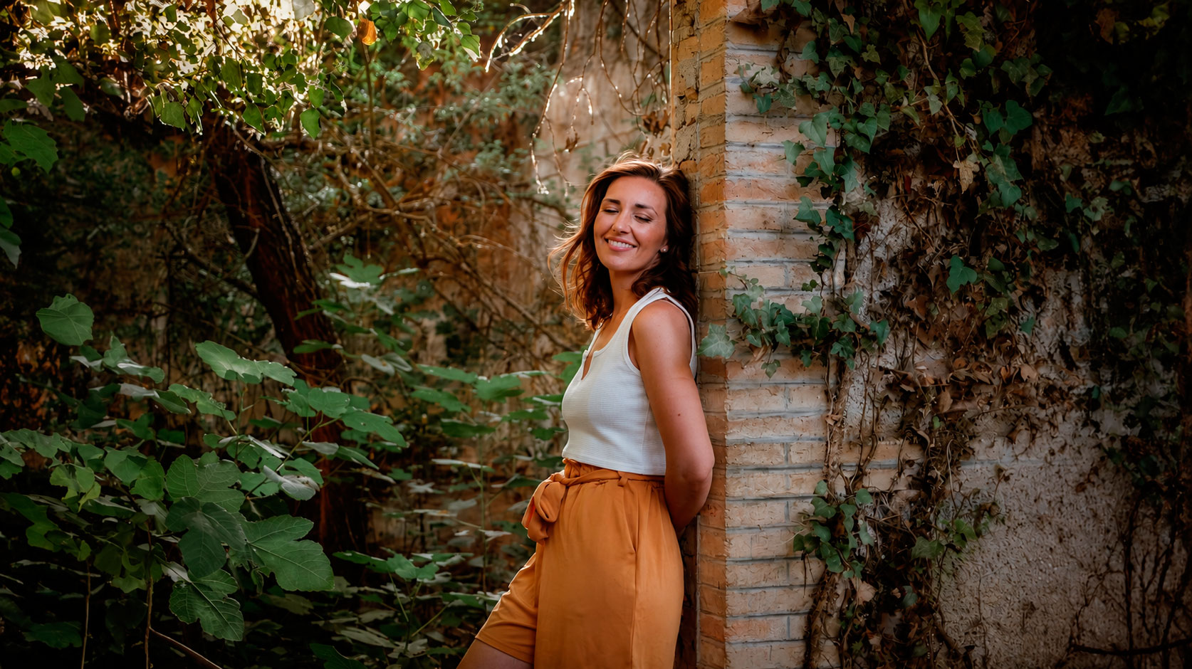 Nieves Espigares sonriendo, apoyada en un muro cubierto de hiedra en un jardín